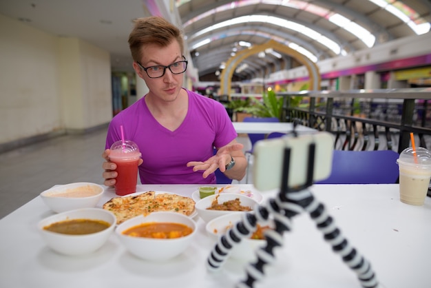 Joven vlogging con teléfono móvil en restaurante indio