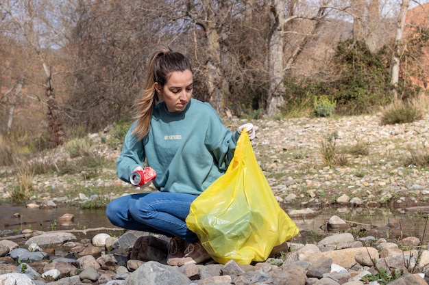 Una joven voluntaria agachada recoge basura de la orilla del río