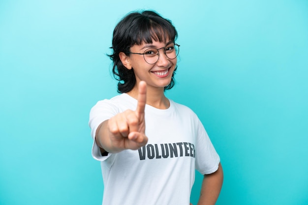 Joven voluntaria argentina aislada de fondo azul mostrando y levantando un dedo