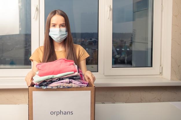 Una joven voluntaria con una caja de ropa para niños huérfanos en el centro de ayuda