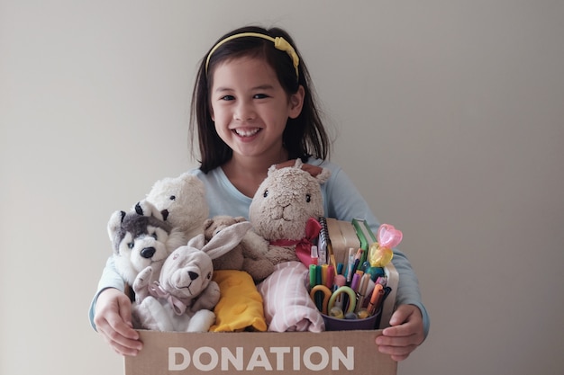 Foto joven voluntaria mixta sosteniendo una caja llena de juguetes usados