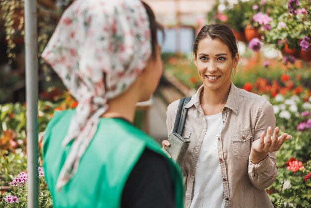 Joven voluntaria de vivero de plantas ayuda a una mujer joven a elegir y comprar flores.