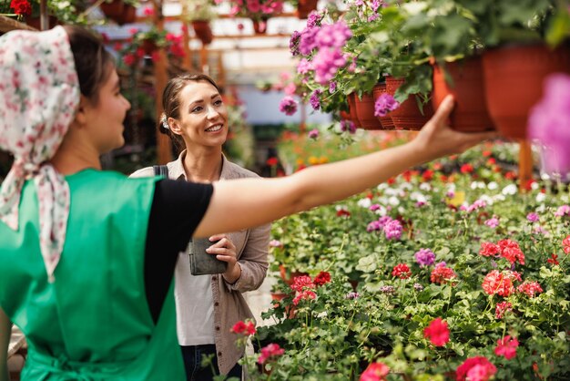 Joven voluntaria de vivero de plantas ayuda a una mujer joven a elegir y comprar flores.