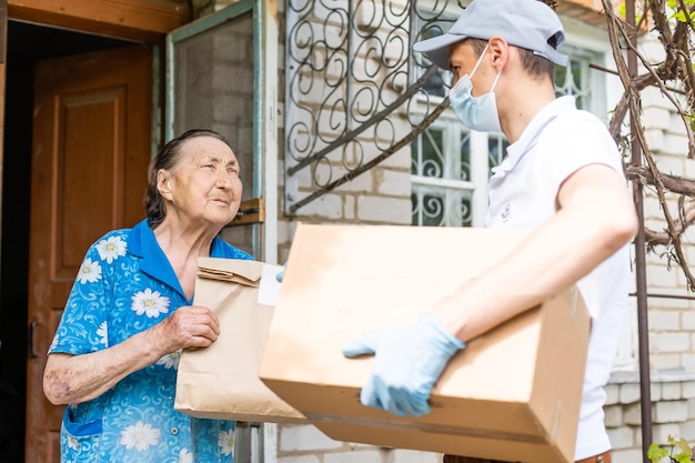 Foto un joven voluntario enmascarado le da a una anciana cajas con comida cerca de su casa. el hijo ayuda a una madre anciana soltera. apoyo familiar, cuidado. en cuarentena, aislado. coronavirus (covid-19. donación