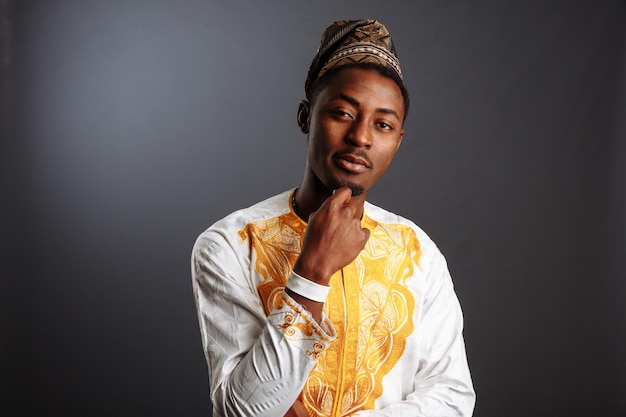 Joven en yoruba y ropa nacional blanca y dorada de pie y posando en fondo gris