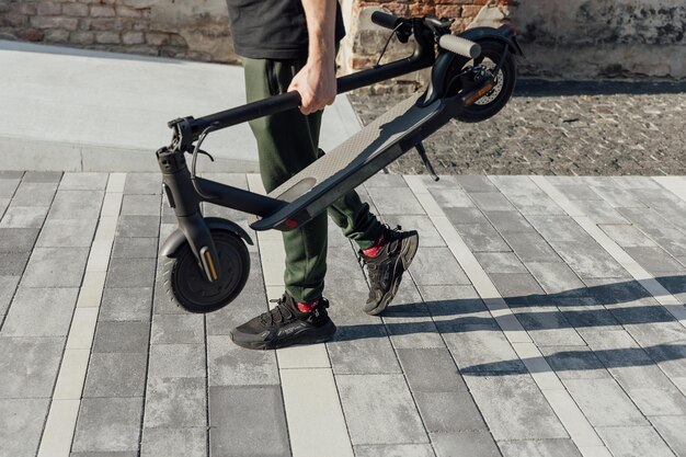 Joven en zapatillas negras con scooter eléctrico doblado