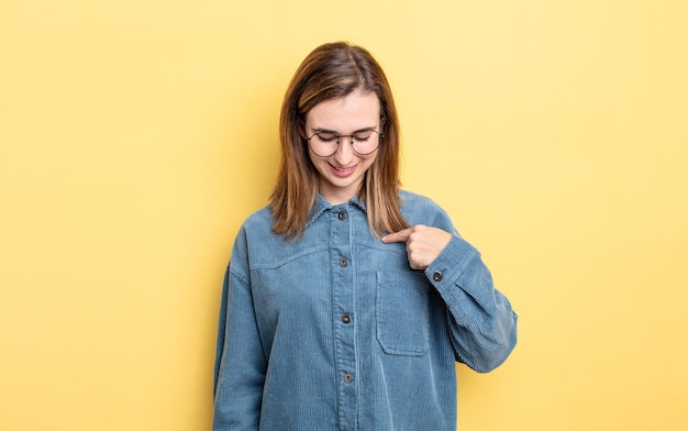 jovencita bonita sonriendo alegre y casualmente, mirando hacia abajo y apuntando al pecho