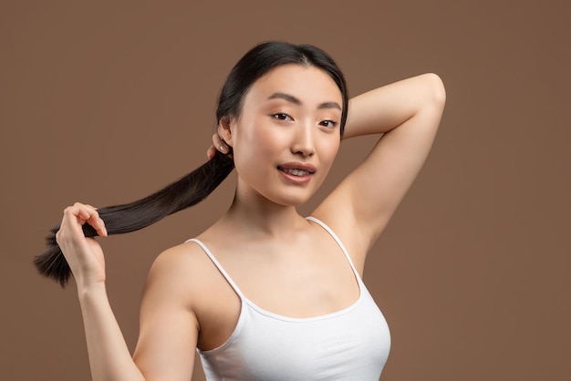 Jovencita coreana con una piel perfecta que muestra su cabello largo y sedoso posando en un estudio marrón