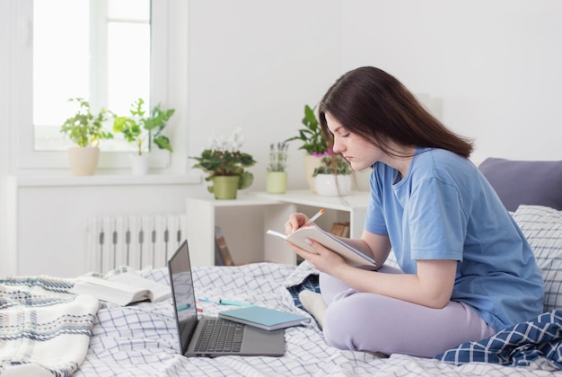 Jovencita estudiando en casa en la cama con una laptop