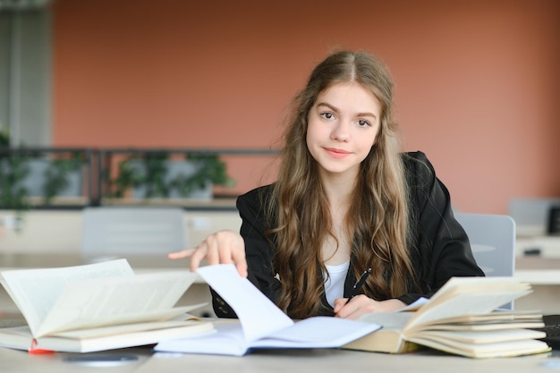 Jovencita estudiando con libros de texto escribiendo ensayos aprendiendo en el aula