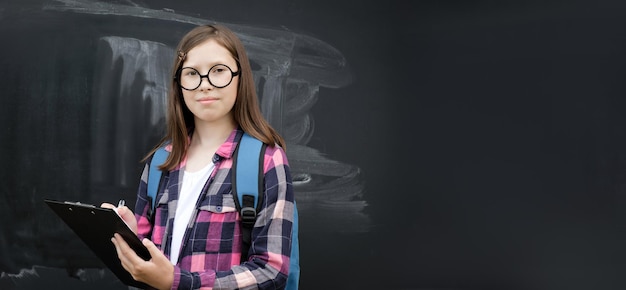 Jovencita estudiante pequeña sosteniendo libros de pila Fondo de pizarra Gafas adolescentes Escuela de educación