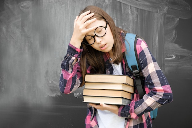 Jovencita estudiante sosteniendo un montón de libros pesados con fondo de pizarra