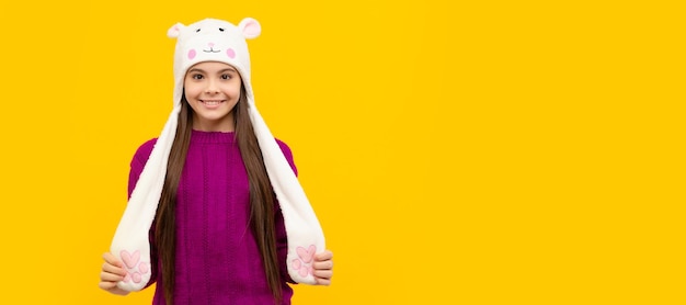 Jovencita en géneros de punto expresa emoción positiva niño positivo en sombrero con orejeras Banner de navidad niño niña estudio niño retrato de invierno con espacio de copia