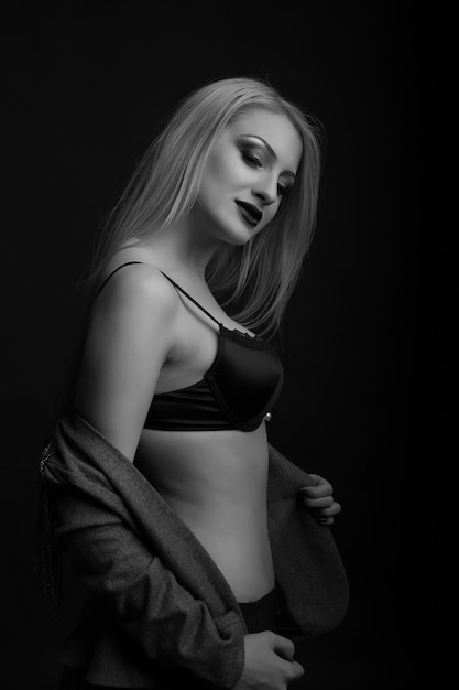 Jovencita glamorosa viste sujetador y chaqueta posando en el estudio oscuro. Disparo monocromo