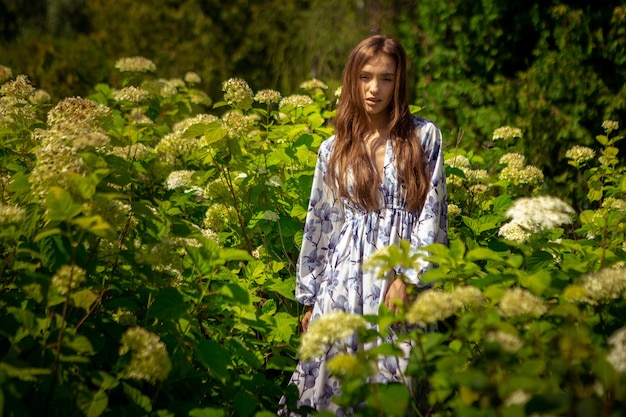 Jovencita de glamour con los ojos cerrados posando en el campo de flores en vestido con estampado