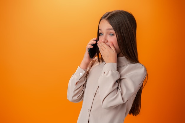 Jovencita hablando por teléfono celular aislado sobre fondo naranja