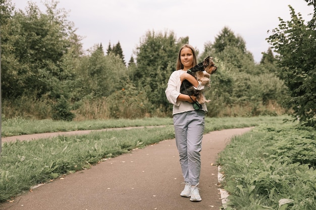 Jovencita en un paseo por el parque de verano con su mascota Yorkshire terrier. Niño paseando a un perro