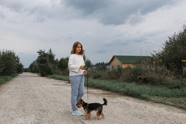 Jovencita en un paseo por el parque de verano con su mascota Yorkshire terrier. Niño paseando a un perro