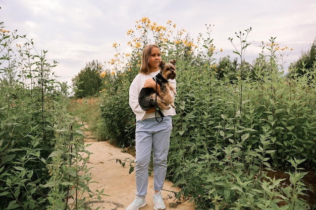 Jovencita en un paseo por el parque de verano con su mascota Yorkshire terrier. Niño paseando a un perro