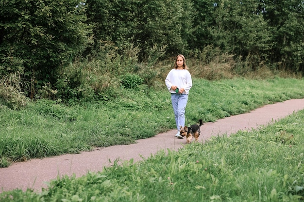 Jovencita en un paseo por el parque de verano con su mascota Yorkshire terrier. Niño paseando a un perro