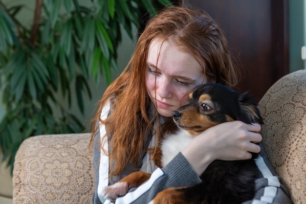 Jovencita pelirroja, generación Z, llorando en casa abrazada a un perro