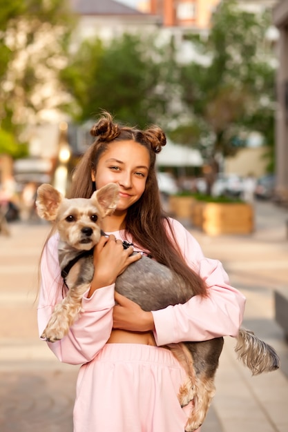 Jovencita con perro pequeño animal de compañía sosteniendo en manos al aire libre en un parque.