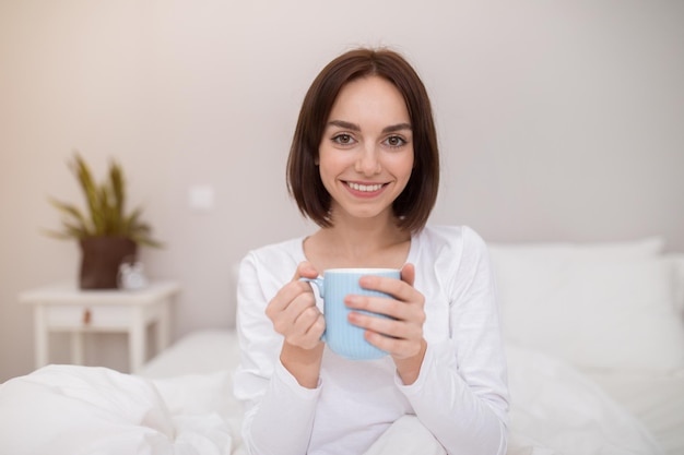 Jovencita positiva disfrutando de un café fresco por la mañana en casa