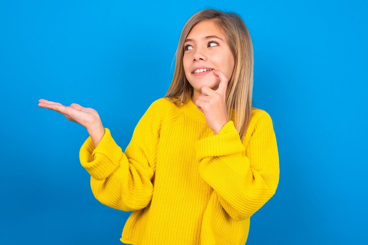 Foto una jovencita positiva que usa un suéter amarillo promociona un anuncio toca los dientes con el dedo