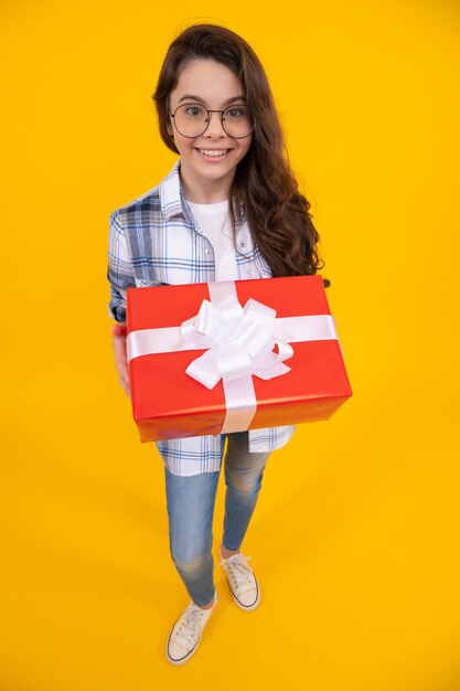 Una jovencita positiva sosteniendo una caja de una jovencita presente con un presente aislado de fondo amarillo