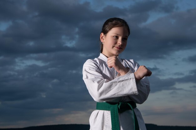 Jovencita practicando karate adolescente niño luchador sobre fondo de cielo adolescente tiene cinturón verde