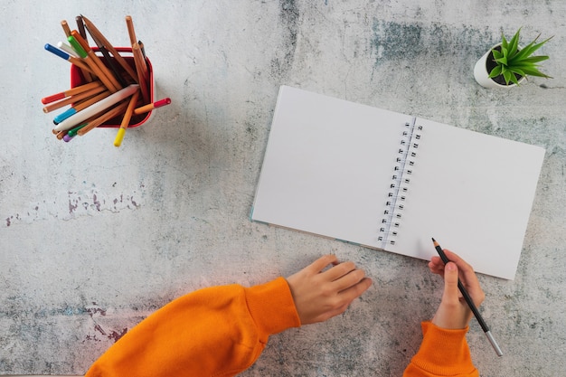 Una jovencita preparada para dibujar en el álbum. Sobre la mesa hay lápices de colores, cuaderno, manos.