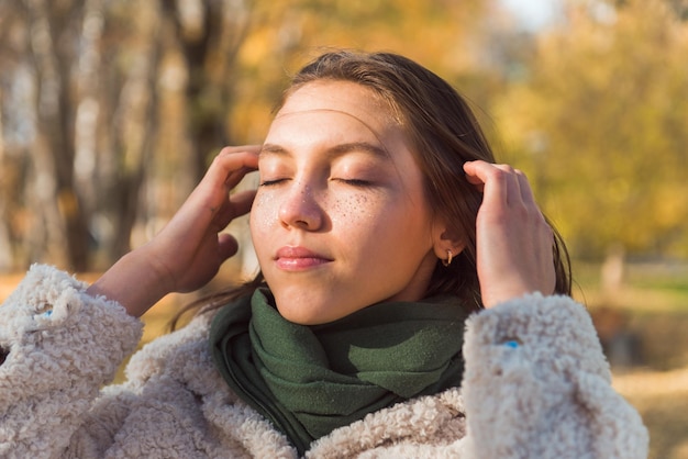 Jovencita retrato de otoño al aire libre con los ojos cerrados a la luz del sol