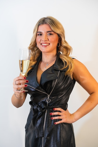 Jovencita rubia con un elegante vestido negro posando con una copa de champán