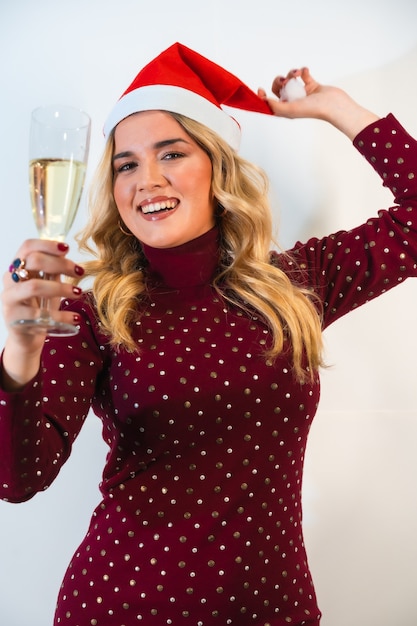 Jovencita rubia con un gorro de Papá Noel posando con una copa de champán