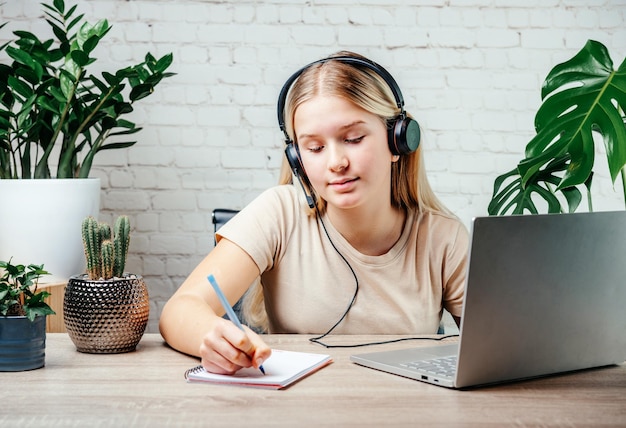 Foto jovencita rubia usando audífonos estudiando en línea con el profesor de skype de chat de internet