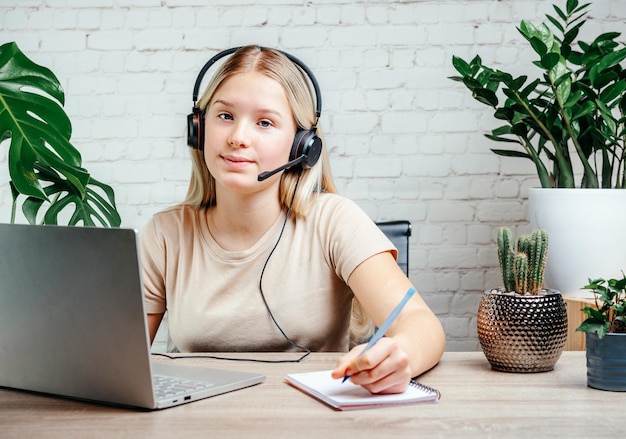 Jovencita rubia usando audífonos estudiando en línea con profesor de skype de chat de internet