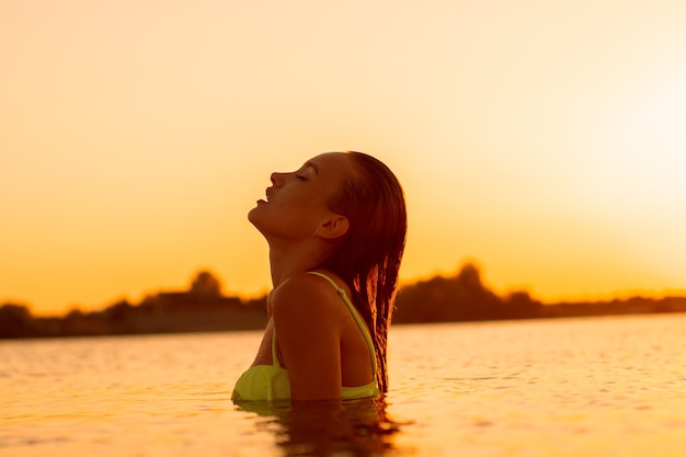 Jovencita sexual en el mar al atardecer cálido