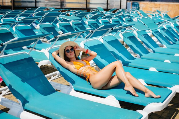 Una jovencita sexy con gafas y un sombrero está sonriendo felizmente y tomando el sol en una tumbona en un día soleado. Felices vacaciones vacaciones. Vacaciones de verano y turismo.