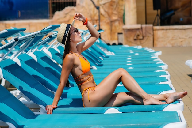 Una jovencita sexy con gafas y un sombrero está sonriendo felizmente y tomando el sol en una tumbona en un día soleado. Felices vacaciones vacaciones. Vacaciones de verano y turismo.