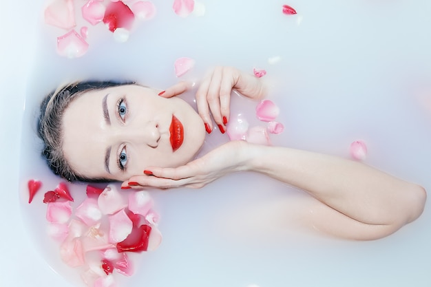 Foto jovencita sexy tomando un baño de leche con pétalos de rosa