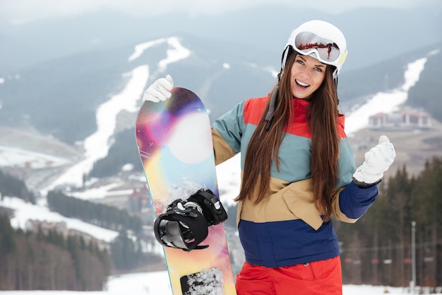 Jovencita snowboarder en las laderas día de invierno helado sosteniendo snowboard en las manos