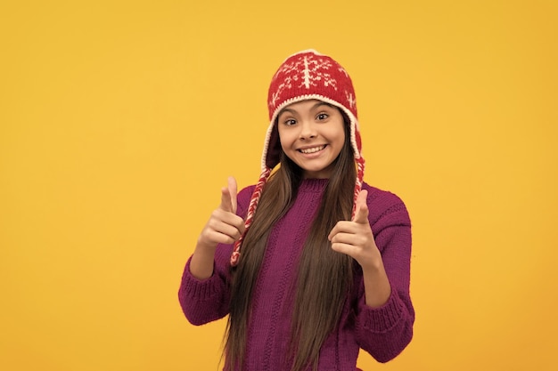 Una jovencita sonriente usa gorro de punto con el dedo acusador para mantenerse caliente