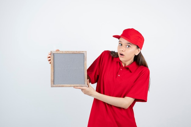 Jovencita en uniforme rojo de pie y sosteniendo el bastidor