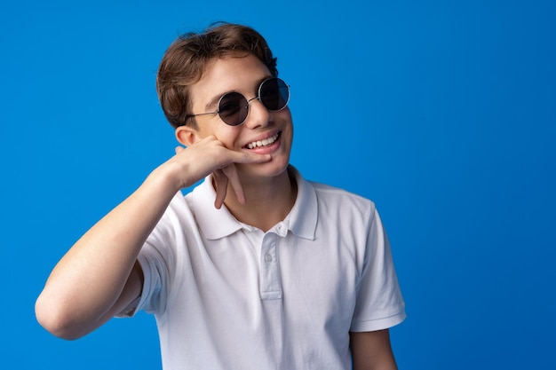 Jovencito en gafas y camisa aislado sobre fondo azul.