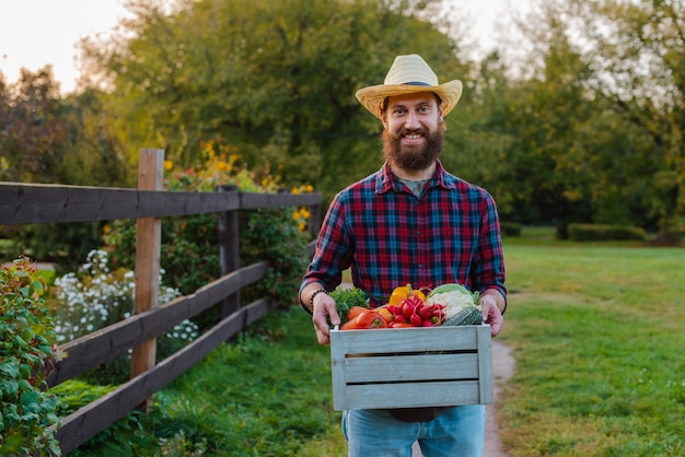 Jóvenes de 30-35 años de edad, barbudo joven hombre agricultor sombrero masculino con caja de huerto ecológico fresco