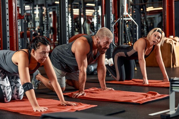 Los jóvenes y activos en el entrenamiento deportivo grupal juntos hacen calentamiento y hacen ejercicio para estirar los brazos La gente entrena en un amplio y luminoso gimnasio Concepto de deporte y estilo de vida saludable