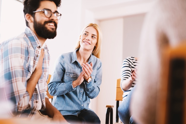 Foto jóvenes adictos que celebran la situación mientras están sentados juntos en terapia de grupo especial. chico guapo hipster sonriendo después de su confesión y progreso.