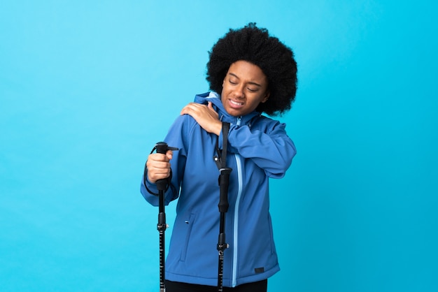 Jóvenes africanos americanos con mochila y bastones de trekking aislado sobre fondo azul.