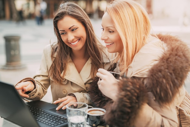 Jóvenes amigas alegres en el café del jardín disfrutando con una laptop y café.