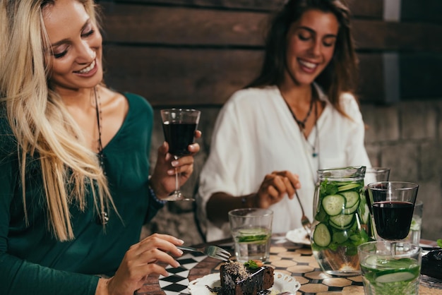 Jóvenes amigas comiendo pasteles y bebiendo vino